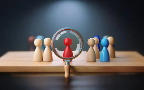 A magnifying glass focuses on a single red game piece, highlighting it amidst a group of other game pieces.