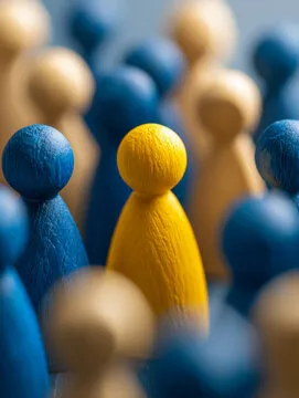 A yellow wooden figurine standing out prominently among many blue and beige wooden figurines symbolizing individuality and uniqueness in a crowd