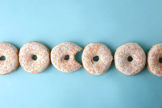 Bitten doughnut among whole ones on color background. Concept of uniqueness